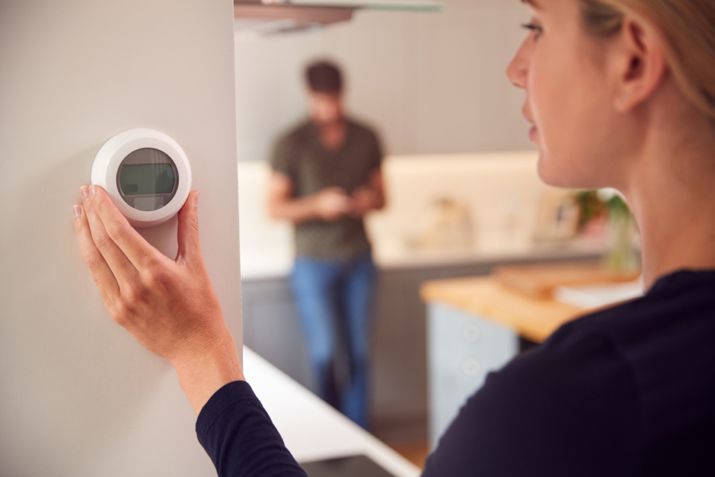Close Up Of Woman Adjusting Wall Mounted Digital Central Heating Thermostat Control At Home